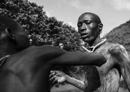 Shepherd From Suri Tribe Receiving Help To Decorate His Body With Camouflage Paintings Before Leaving The Village, Tulgit, Omo Valley, Ethiopia