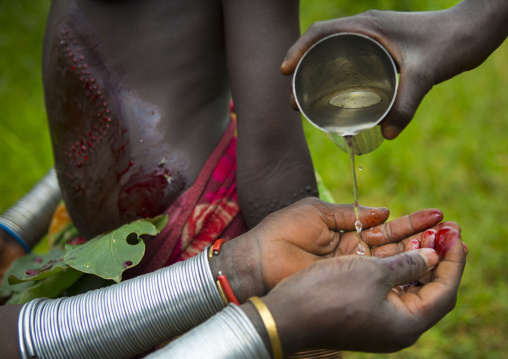 Suri woman washing her hands from blood after a scarification ceremony, Tulgit, Omo valley, Ethiopia