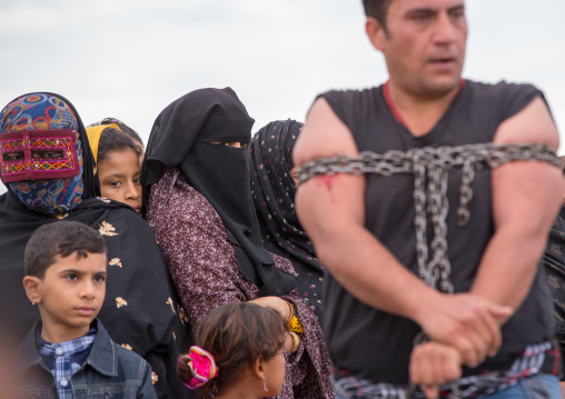 masked women looking at a strongman struggling to break free of chains at the panjshambe bazar, Hormozgan, Minab, Iran