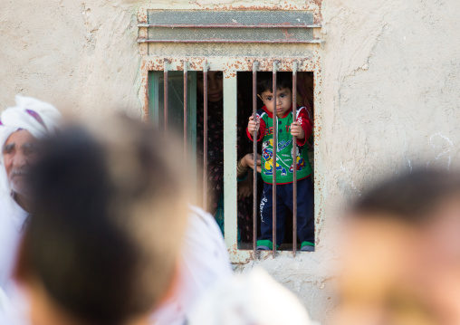 todder boy behing the bars of a window looking in the street, Qeshm Island, Salakh, Iran