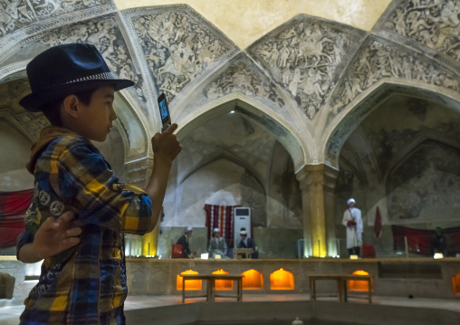 Iranian boy taking pictures with his mobile phone inside the hamman-e vakil bath, Fars province, Shiraz, Iran