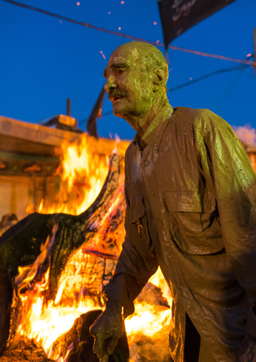 Iranian shiite muslim man standing in front of a bonfire after rubbing mud on his body during the Kharrah Mali ritual to mark the Ashura ceremony, Lorestan Province, Khorramabad, Iran