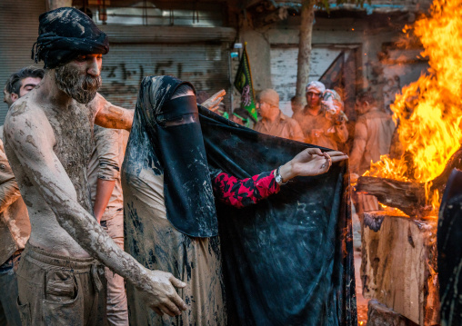 Iranian shiite muslim woman stand in front of  a bonfire after rubbing mud on her chador during the Kharrah Mali ritual to mark the Ashura day, Lorestan Province, Khorramabad, Iran