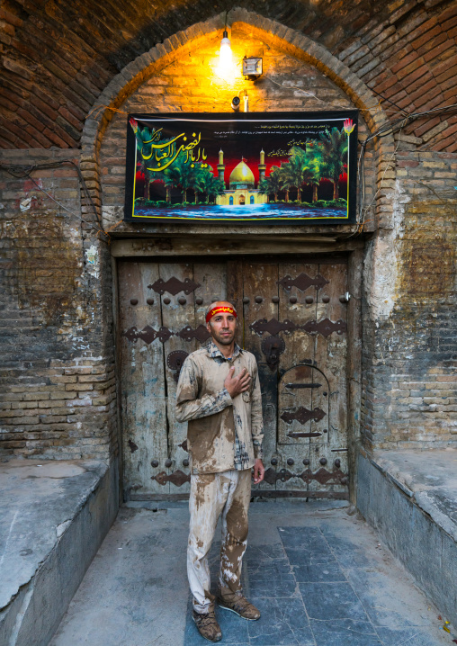 Iranian shiite muslim man standing in front of an old wooden door after rubbing mud on his clothes during the Kharrah Mali ritual to mark the Ashura ceremony, Lorestan Province, Khorramabad, 