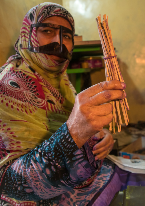 a bandari woman with a traditional mask and showing palm trees branches she uses for the mask, Qeshm Island, Salakh, Iran