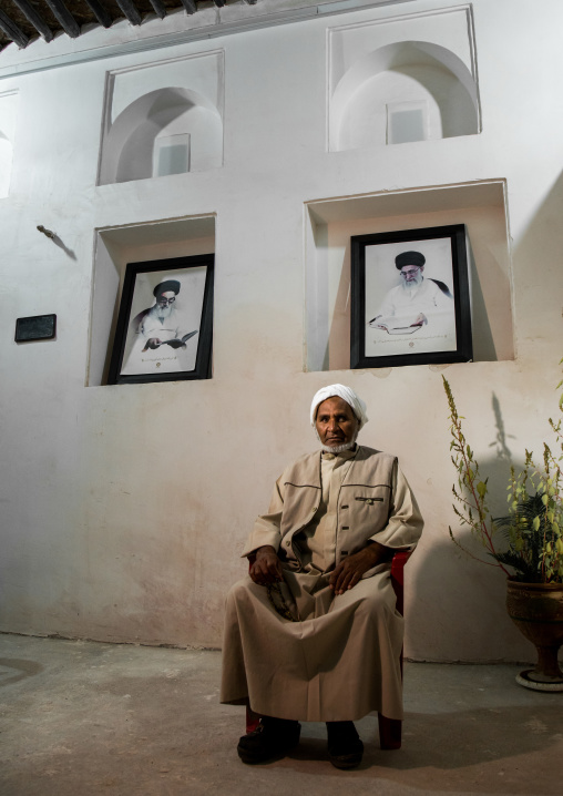 old bandari sailor in front of khameini and khomeini portraits in a house, Hormozgan, Bandar-e Kong, Iran