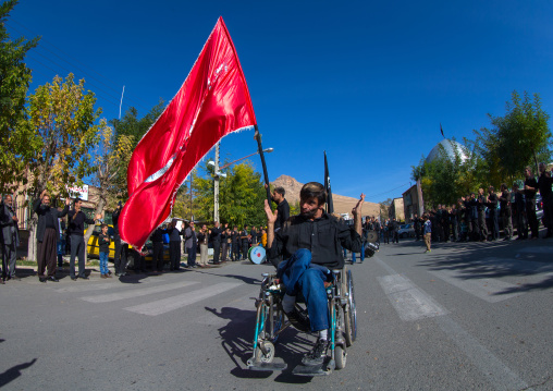 Man In Wheelchair In Front Of A Red Flag Celebrating Ashura, The Day Of The Death Of Imam Hussein, Kurdistan Province, Bijar, Iran