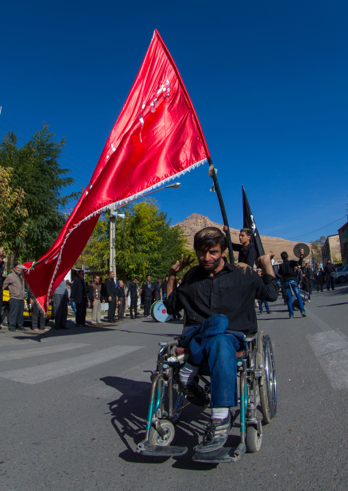 Man In Wheelchair In Front Of A Red Flag Celebrating Ashura, The Day Of The Death Of Imam Hussein, Kurdistan Province, Bijar, Iran