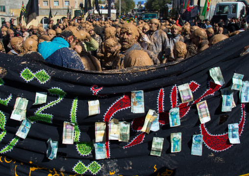 Iranian Shiite Muslim Men Covered In Mud In Front Of A Flag With Bank Notes Attached During Ashura Day, Kurdistan Province, Bijar, Iran