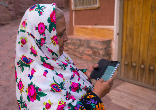 Portrait Of An Iranian Woman Wearing Traditional Floreal Chador And Texting On Her Mobile Phone, Isfahan Province, Abyaneh, Iran