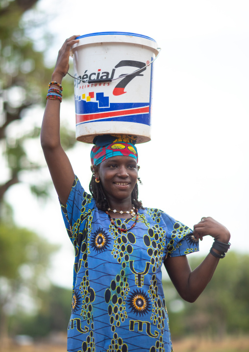 Portrait of a Peul tribe girl carrying a bucket full of water on the head, Savanes district, Boundiali, Ivory Coast