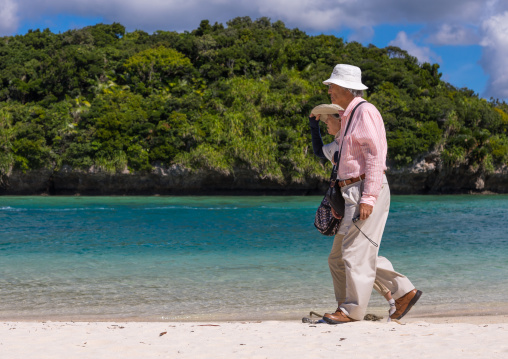 Old japanese couple walking along the tropical lagoon with clear blue water in Kabira bay, Yaeyama Islands, Ishigaki, Japan