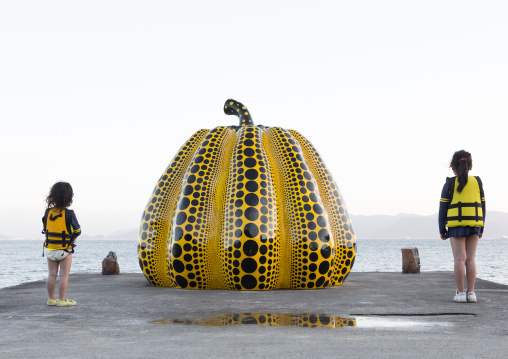 Children standing on the sides of the yellow pumpkin by Yayoi Kusama on pier at sea, Seto Inland Sea, Naoshima, Japan