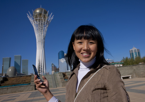 Ethnic Kazakh Girl With Cellphone In Front Of Baiterek Tower, Astana, Kazakhstan"