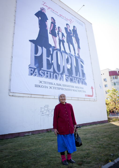 Old Woman In Front Of An Advertising Poster For A Fashion School, Astana, Kazakhstan