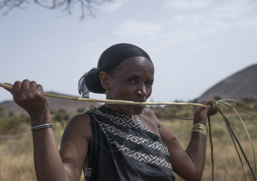 Borana woman cutting wood with her teeth to build a house, Marsabit district, Marsabit, Kenya