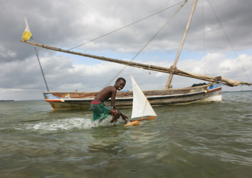 Young boy playing with dhow model along seashore, Lamu County, Lamu, Kenya