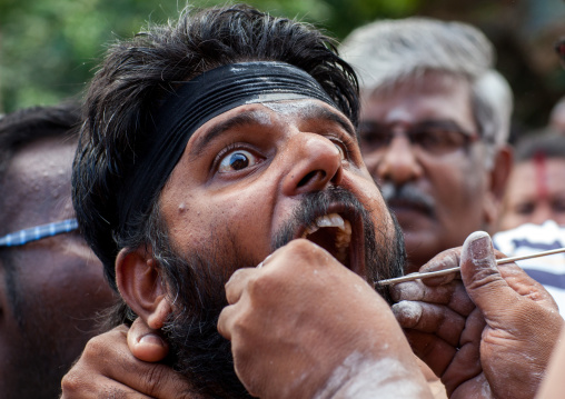 A Devotee Cheek Is Pierced With A Skewer By A Priest At Thaipusam Hindu Festival At Batu Caves, Southeast Asia, Kuala Lumpur, Malaysia