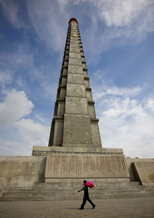 North Korean man going to a parade with flowers passing in front of Juche tower, Pyongan Province, Pyongyang, North Korea