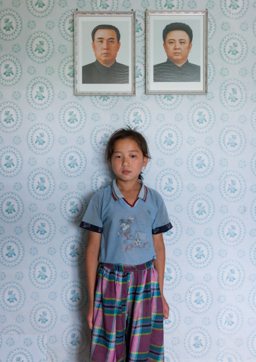 North Korean girl posing below the portraits of the Dear Leaders inside her home, Kangwon Province, Chonsam Cooperative Farm, North Korea