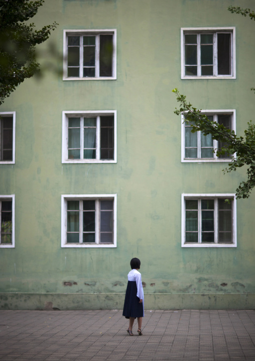 North Korean woman passing in front of a green apartments building, Pyongan Province, Pyongyang, North Korea