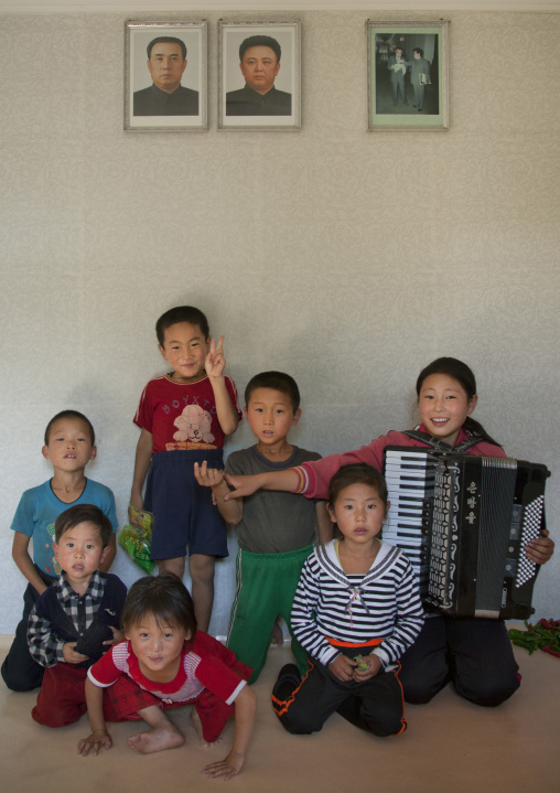 Group of children posing under Kim Jong il and Kim il Sung portraits in a house, South Pyongan Province, Chonsam Cooperative Farm, North Korea