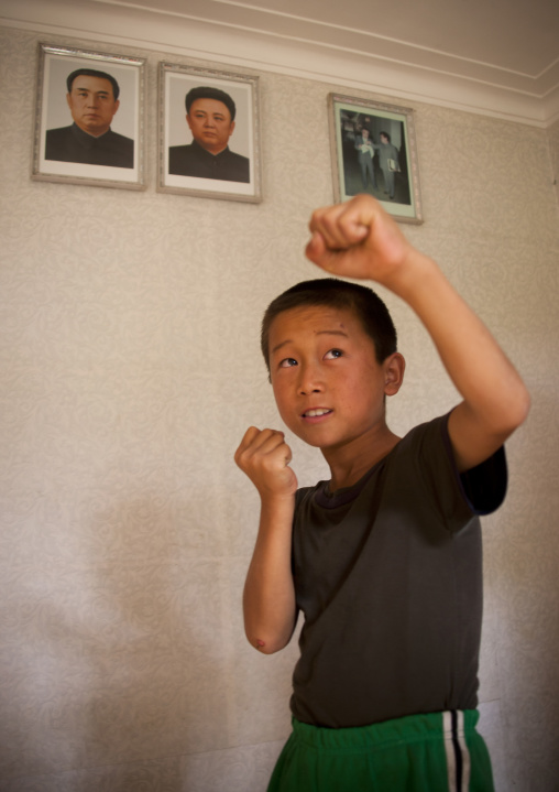 North Korean child doing taekwondo under the portraits of Kim il Sung and Kim Jong il, South Pyongan Province, Chonsam Cooperative Farm, North Korea