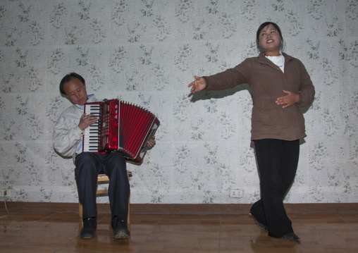 North Korean woman singing with a man playing accordion in a homestay, North Hamgyong Province, Jung Pyong Ri, North Korea