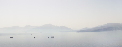 Dhows sailing in the fjords in front of mountains in the morning, Musandam Governorate, Khasab, Oman