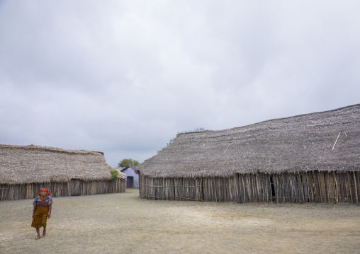 Panama, San Blas Islands, Mamitupu, Kuna Indian Woman Pssing In Front Of Typical Homes With Thatched Roofs