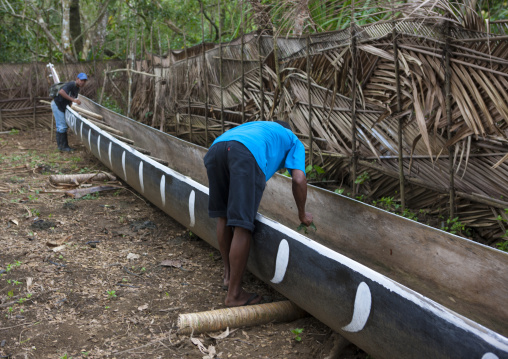 Man wotking on a traditional canoe with carved and painted decorations, Milne Bay Province, Alotau, Papua New Guinea