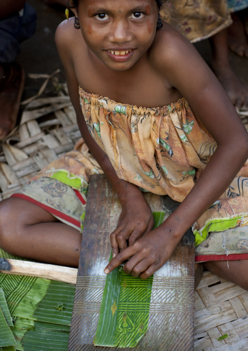 Girl making Doba traditional money with banana leaves on a wooden board, Milne Bay Province, Trobriand Island, Papua New Guinea