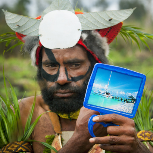 Hagener warrior putting makeup on his face and looking in a mirror, Western Highlands Province, Mount Hagen, Papua New Guinea