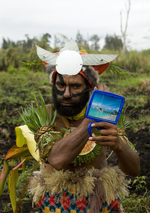 Hagener warrior putting makeup on his face and looking in a mirror, Western Highlands Province, Mount Hagen, Papua New Guinea