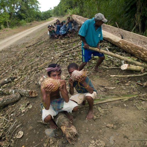 Boys blowing in shells to call people to help making a canoe, Milne Bay Province, Alotau, Papua New Guinea