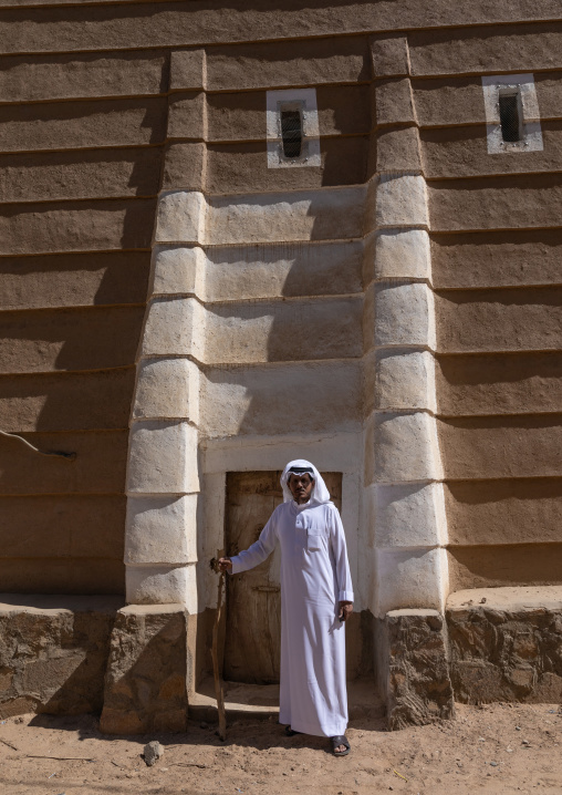 Saudi man standing in front of a traditional old mud house, Najran Province, Najran, Saudi Arabia