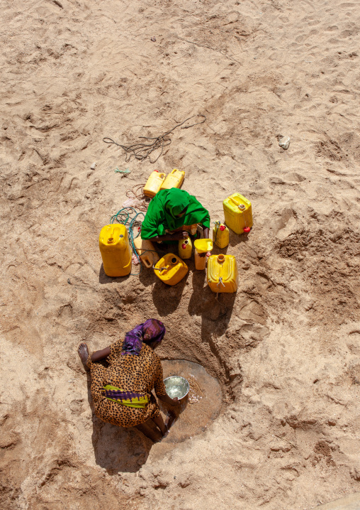 Somali women taking drinking water from a well hole in the sand and pouring it into plastic containers, North-Western province, Lasadacwo Village, Somaliland