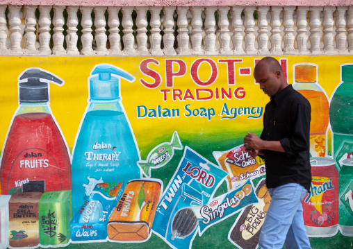 Somali man lokking at his mobile phone and passing in front of a painted bilboard advertisement, Woqooyi Galbeed province, Baligubadle, Somaliland