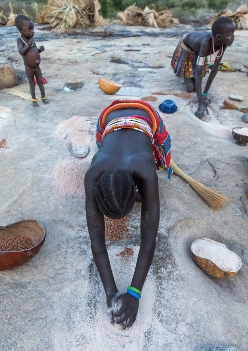 Larim tribe women grinding Sorghum grains in holes in a rock, Boya Mountains, Imatong, South Sudan