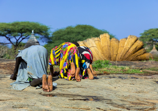 Larim tribe girls grinding sorghum grains in holes in a rock, Boya Mountains, Imatong, South Sudan