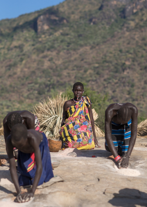 Larim tribe women grinding sorghum grains in holes in a rock, Boya Mountains, Imatong, South Sudan