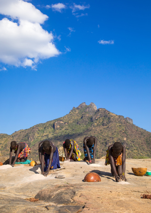 Larim tribe women grinding sorghum grains in holes in a rock, Boya Mountains, Imatong, South Sudan