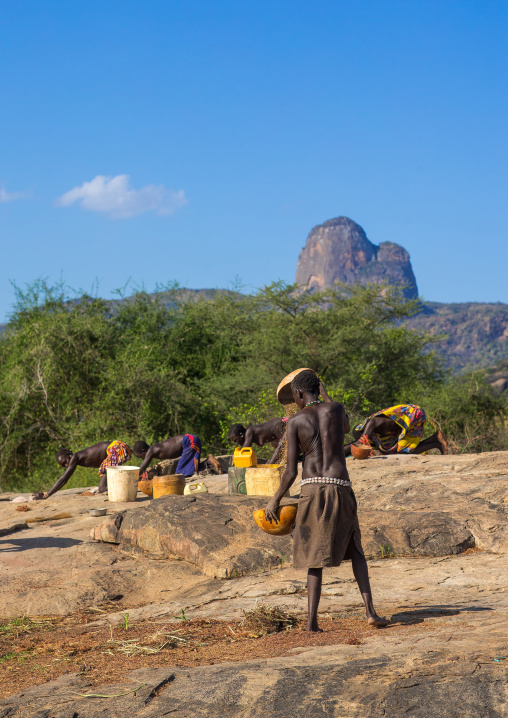 Larim tribe women grinding sorghum grains in holes in a rock, Boya Mountains, Imatong, South Sudan