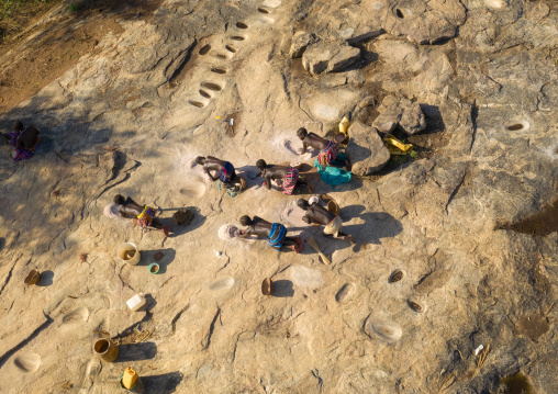 Larim tribe women grinding sorghum grains in holes in a rock, Boya Mountains, Imatong, South Sudan