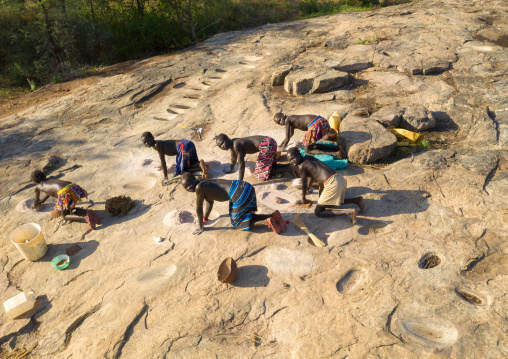 Larim tribe women grinding sorghum grains in holes in a rock, Boya Mountains, Imatong, South Sudan