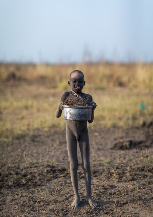 Mundari tribe boy collecting dried cow dungs to make bonfires to repel mosquitoes and flies, Central Equatoria, Terekeka, South Sudan