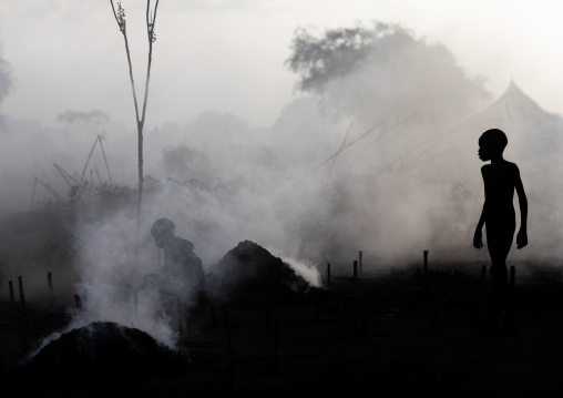 Mundari tribe boy taking care of the bonfires made with dried cow dungs to repel mosquitoes and flies, Central Equatoria, Terekeka, South Sudan