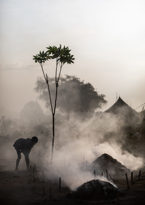 Mundari tribe boy taking care of the bonfires made with dried cow dungs to repel flies and mosquitoes, Central Equatoria, Terekeka, South Sudan