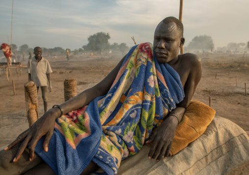 Mundari tribe man resting on a wooden bed in the middle of his long horns cows, Central Equatoria, Terekeka, South Sudan