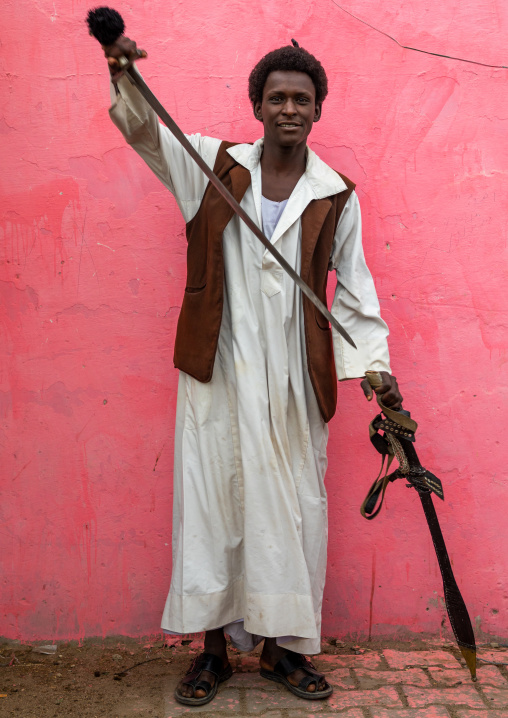 Beja tribe warrior with his sword in front of a pink wall, Red Sea State, Port Sudan, Sudan